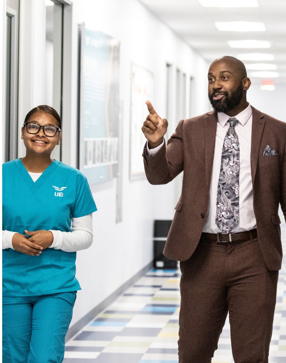 A UEI student and instructor walking down a campus hallway